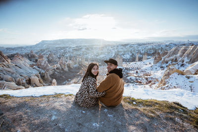 Rear view of woman sitting on rock against sky