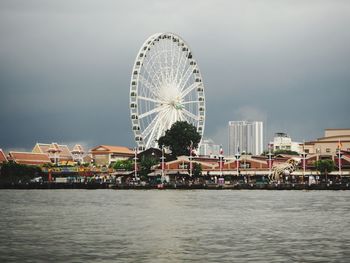 Ferris wheel by river against buildings in city
