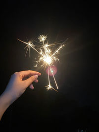 Cropped hand holding sparkler at night