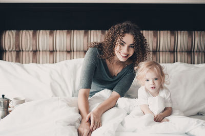 Portrait of young woman and girl on bed at home