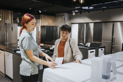 Saleswoman advising female customer in buying washing machine at electronics store