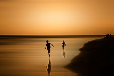 Silhouette people on beach against sky during sunset