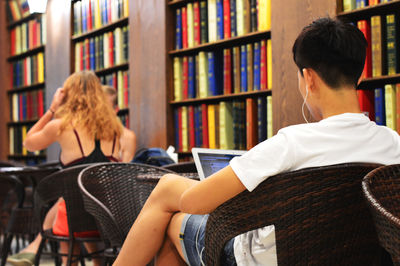 Rear view of man using laptop while sitting on chair in library