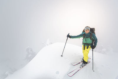 Young woman smiling backcountry skiing on snowy summit in squamish