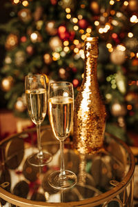 Champagne bottle with golden sequin and glasses at sparkling bokeh yellowish garlands