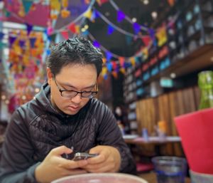 Young asian man using mobile phone at table inside restaurant.