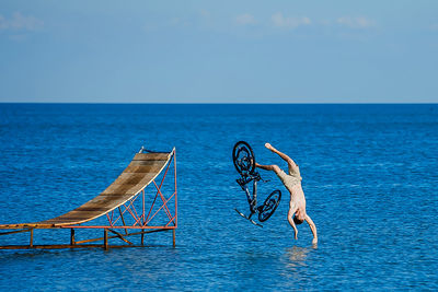 Full length of young man with bicycle diving in sea against sky