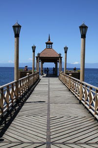 Walkway leading toward gazebo against sky on sunny day