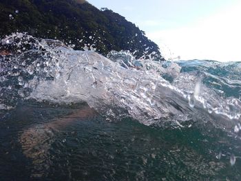 Sea waves splashing on rocks against sky