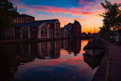 Buildings by lake against sky during sunset