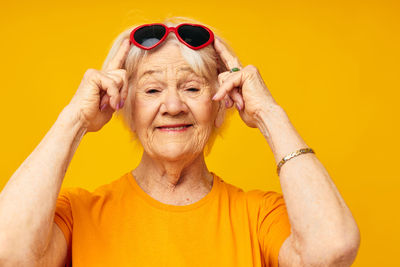 Portrait of young woman wearing sunglasses against yellow background