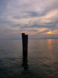 Wooden posts in sea against sky during sunset