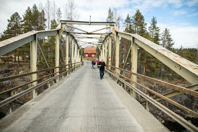 Man walking on footbridge against sky