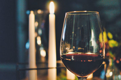 Close-up of wine glass with red wine by burning candles on table at home