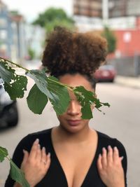 Close-up of leaves against young woman standing on road in city