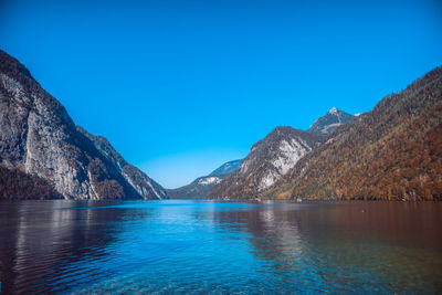 Scenic view of lake and mountains against clear blue sky