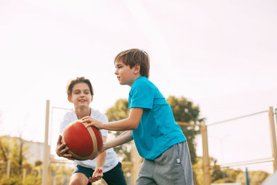 Boys playing basketball against clear sky