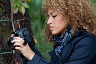 Close-up of young woman photographing by fence