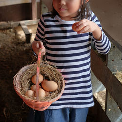 Midsection  of girl holding basket with eggs while standing in pen