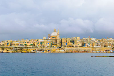 Buildings by sea against cloudy sky