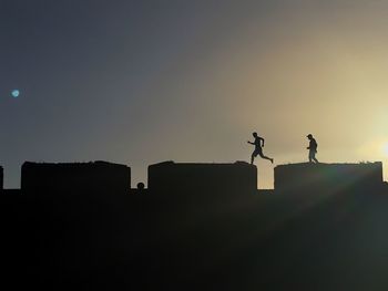 Silhouette people on building against sky during sunset