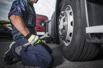 Low section of mechanic holding wrench sitting by tire outdoors