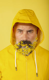 A handsome man in a yellow raincoat with a flower beard on a background a yellow background