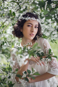 Portrait of a young beautiful woman in white clothes standing next to blooming cherry tree in spring