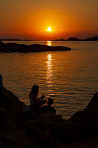 Silhouette man sitting on rocks at beach during sunset