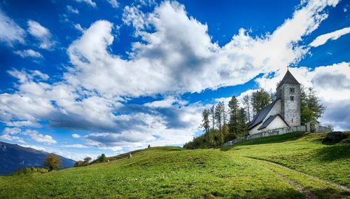 Low angle view of church on grassy hill against cloudy blue sky