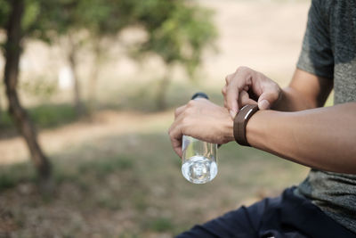 Midsection of man adjusting fitness tracker while sitting outdoors