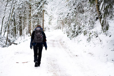 Rear view of woman wearing backpack while walking on snow covered land