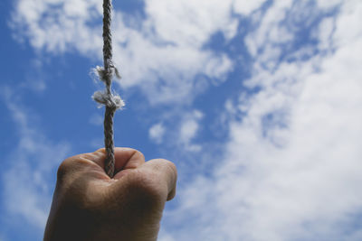 Cropped hand holding string against sky