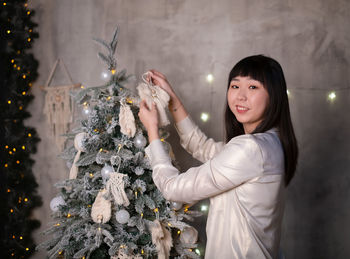 A young, beautiful korean asian woman dresses up a christmas tree with toys 
