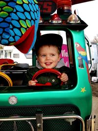 Cheerful boy riding toy car on footpath