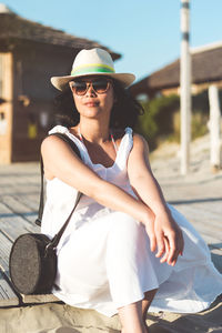 Young woman wearing sunglasses sitting on boardwalk at beach