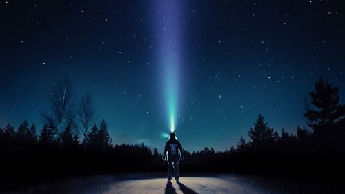 Man standing on illuminated street light against sky at night