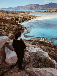 Rear view of woman sitting on rock by sea