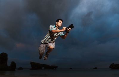 Man with camera levitating over sea against sky at night
