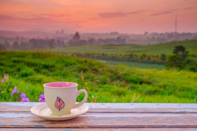 Coffee cup on table by field against sky