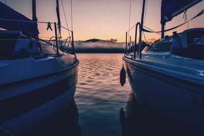 Sailboats moored on sea against sky during sunset