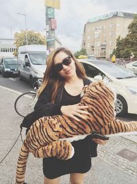 Portrait of woman holding tiger stuffed toy on sidewalk
