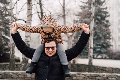 Portrait of happy father with daughter on shoulder outdoors