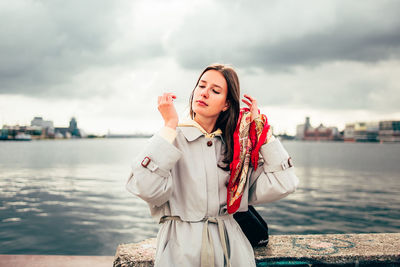 Young woman standing by water against sky