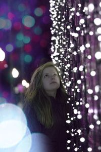 Teenage girl standing by illuminated string lights at night