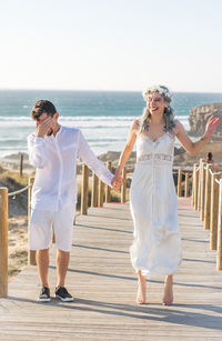 Couple holding hands while standing on footbridge at beach