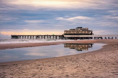 Pier on beach against sky during sunset