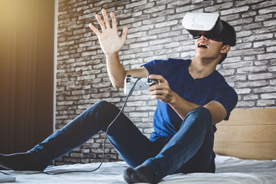 Young man looking through virtual reality simulator while sitting on bed at home