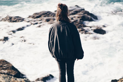 Rear view of woman standing at beach against sea