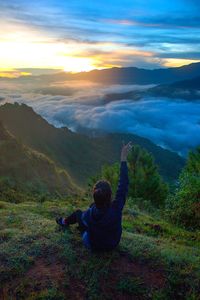 Rear view of woman sitting on mountain against sky